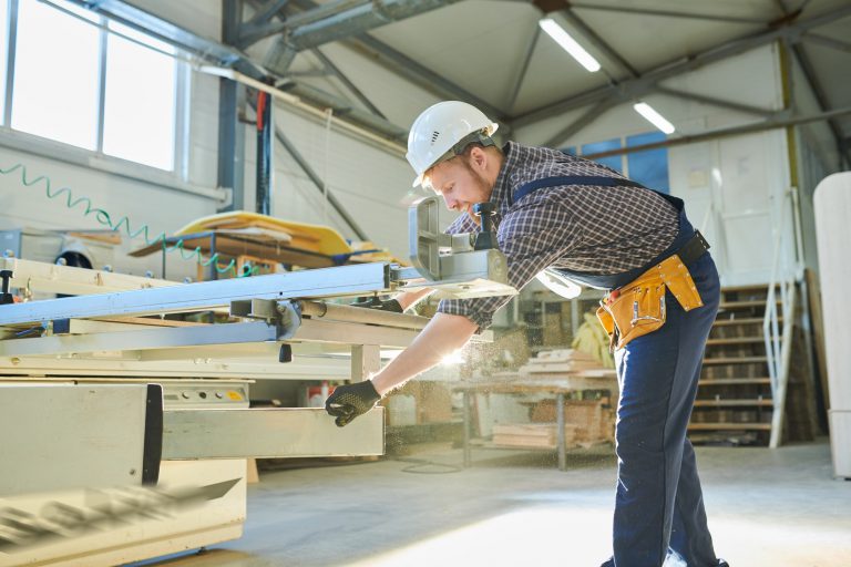 Young worker adjusting assembling machine at furniture plant